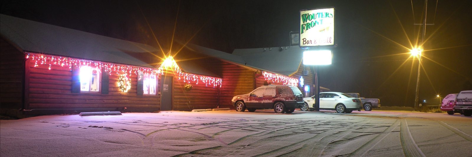 Wouters' Front at night in fresh snow, log-sided walls strung with icicle lights and the hand-painted pole sign lit against a black sky