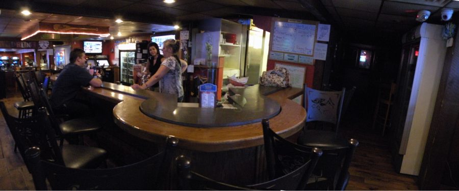The horseshoe bar at Wouters' Front — wooden bar top, black stools, televisions overhead and a neon softball bat on the wall